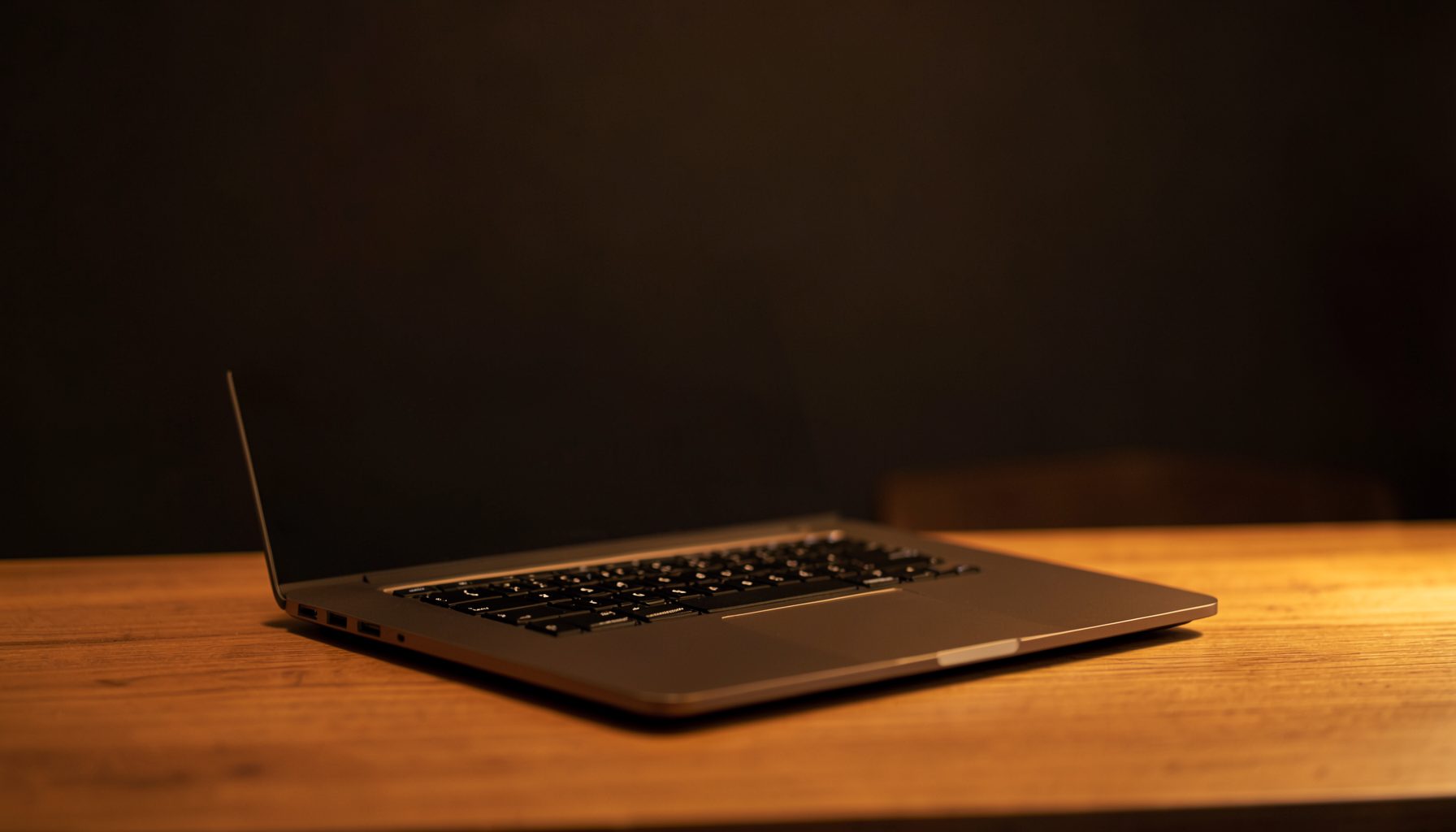 A sleek modern laptop on a wooden desk with warm amber ambient lighting and a dark, minimalist backdrop