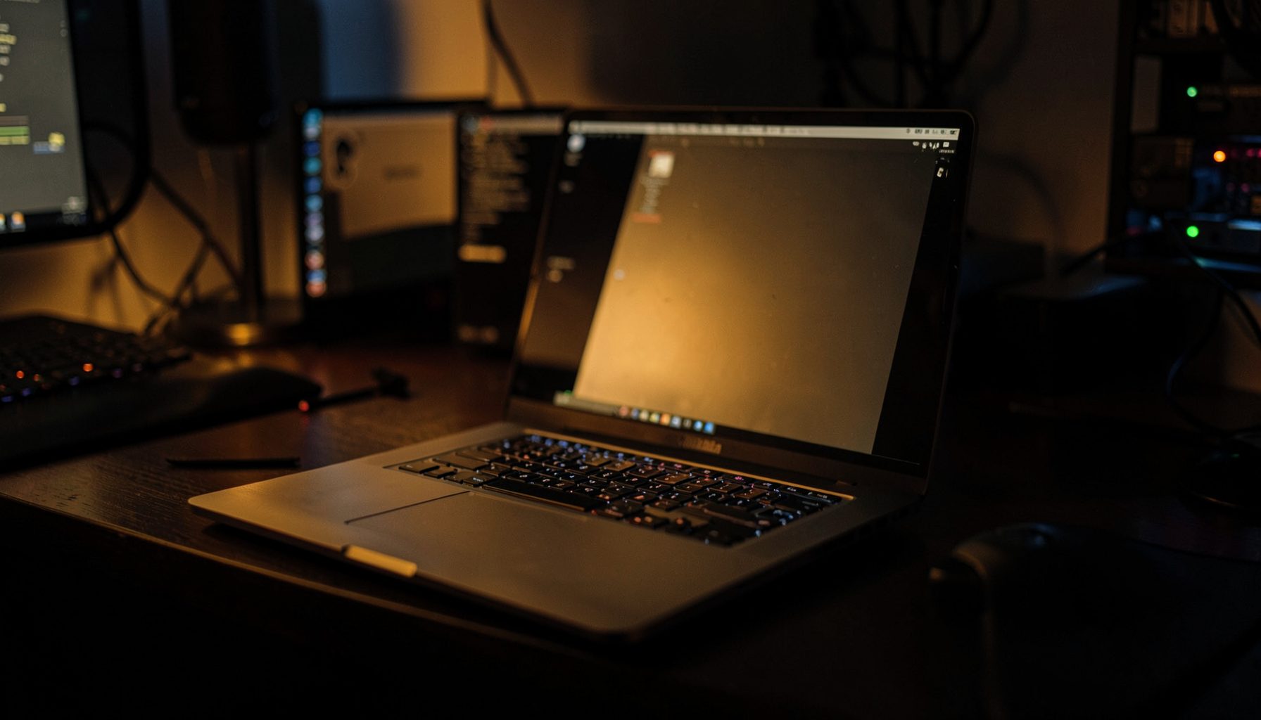 Dark desk setup with a laptop screen glowing in warm amber light, surrounded by soft shadows and a moody tech atmosphere