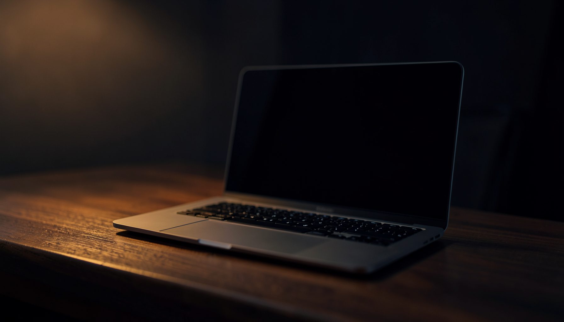 Dark workspace with a sleek laptop on a wooden desk, warm amber and deep navy tones, soft ambient glow