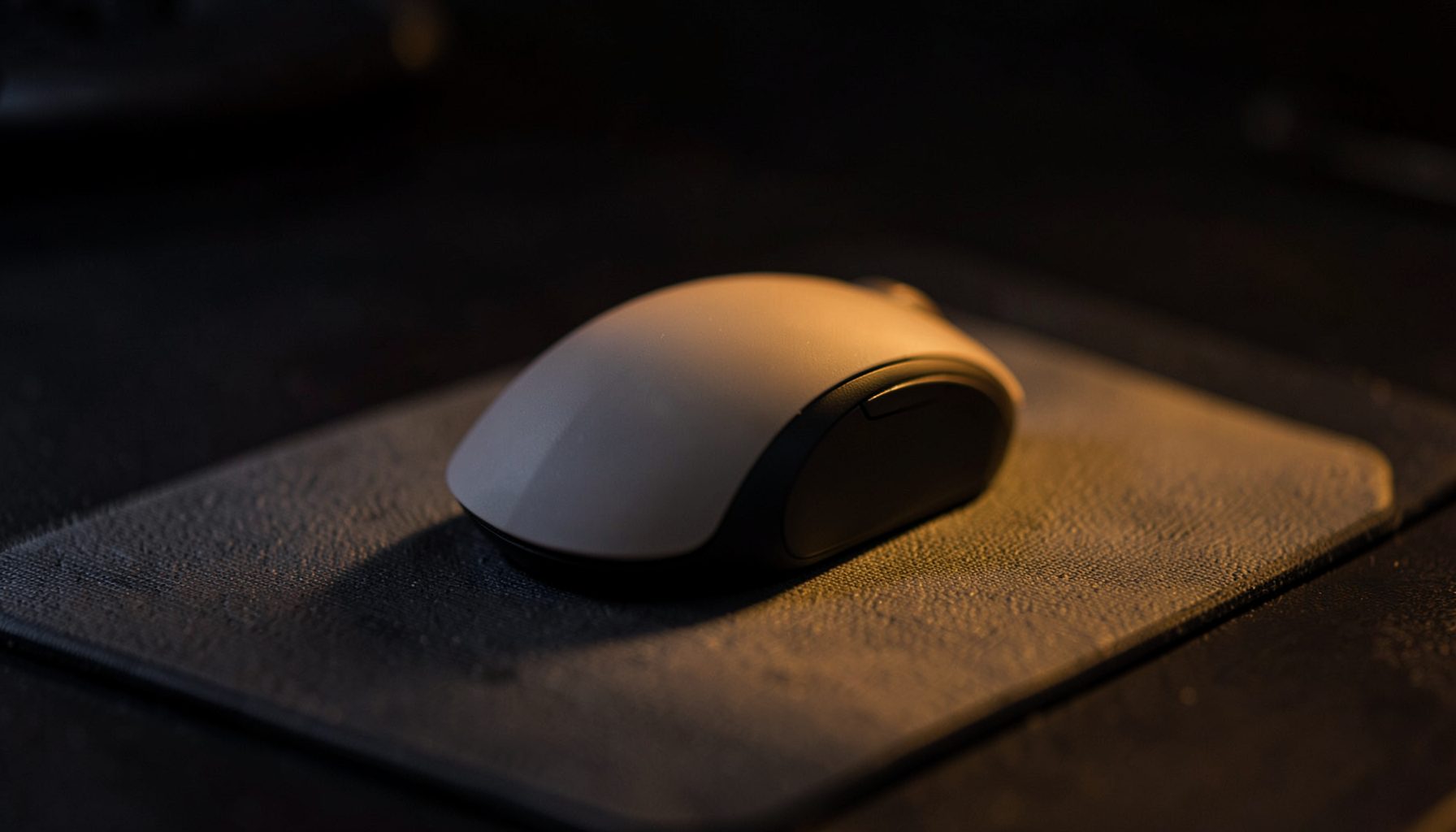 Ergonomic mouse on a desk mat, subtle amber glow against dark background