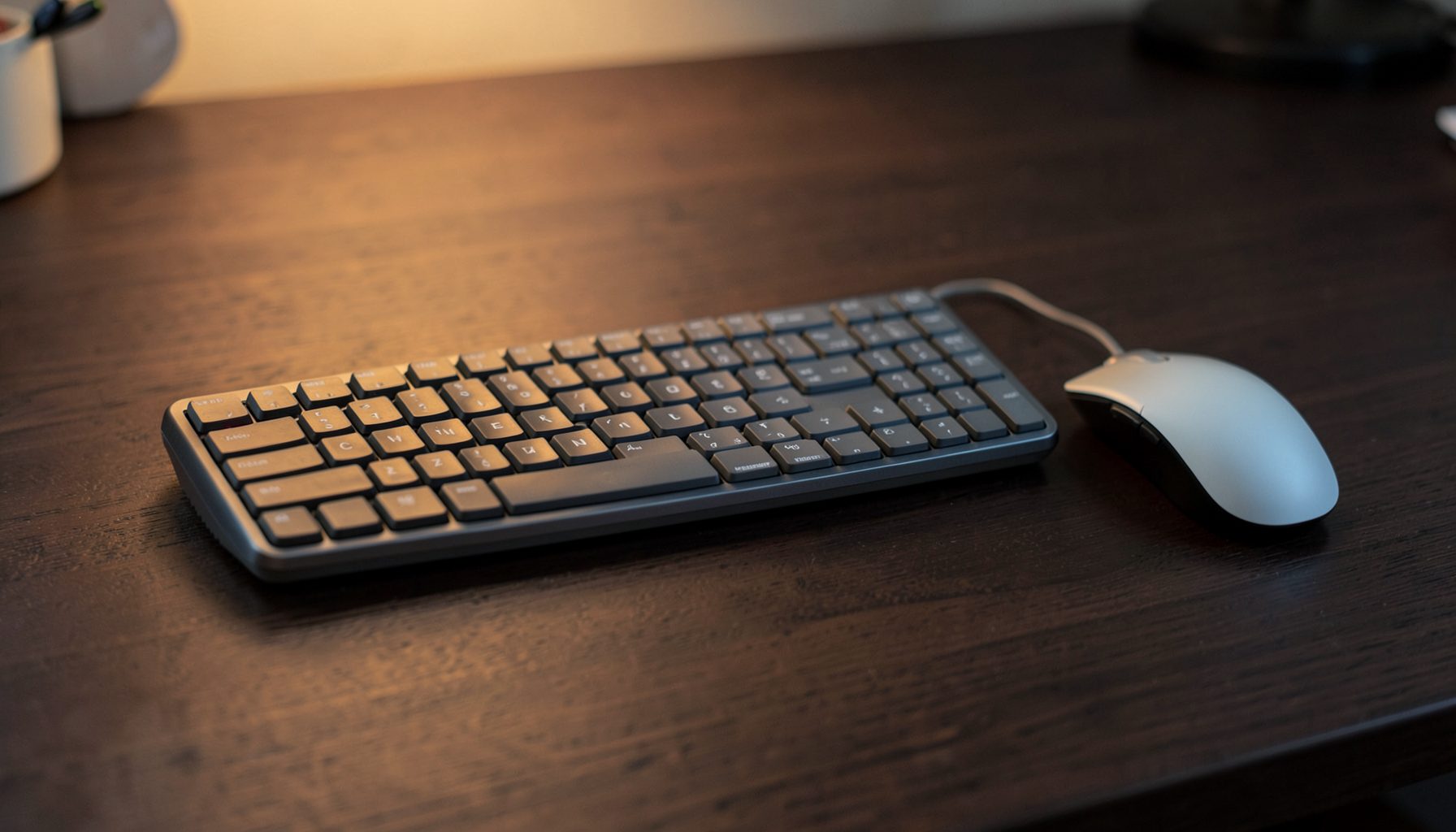 Wireless keyboard and mouse on a clean desk, warm ambient light with dark wood surface